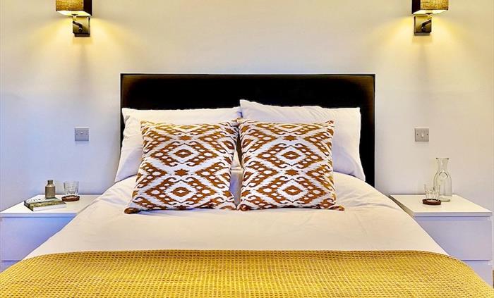 A bed with a colourful throw and decorative cushions.